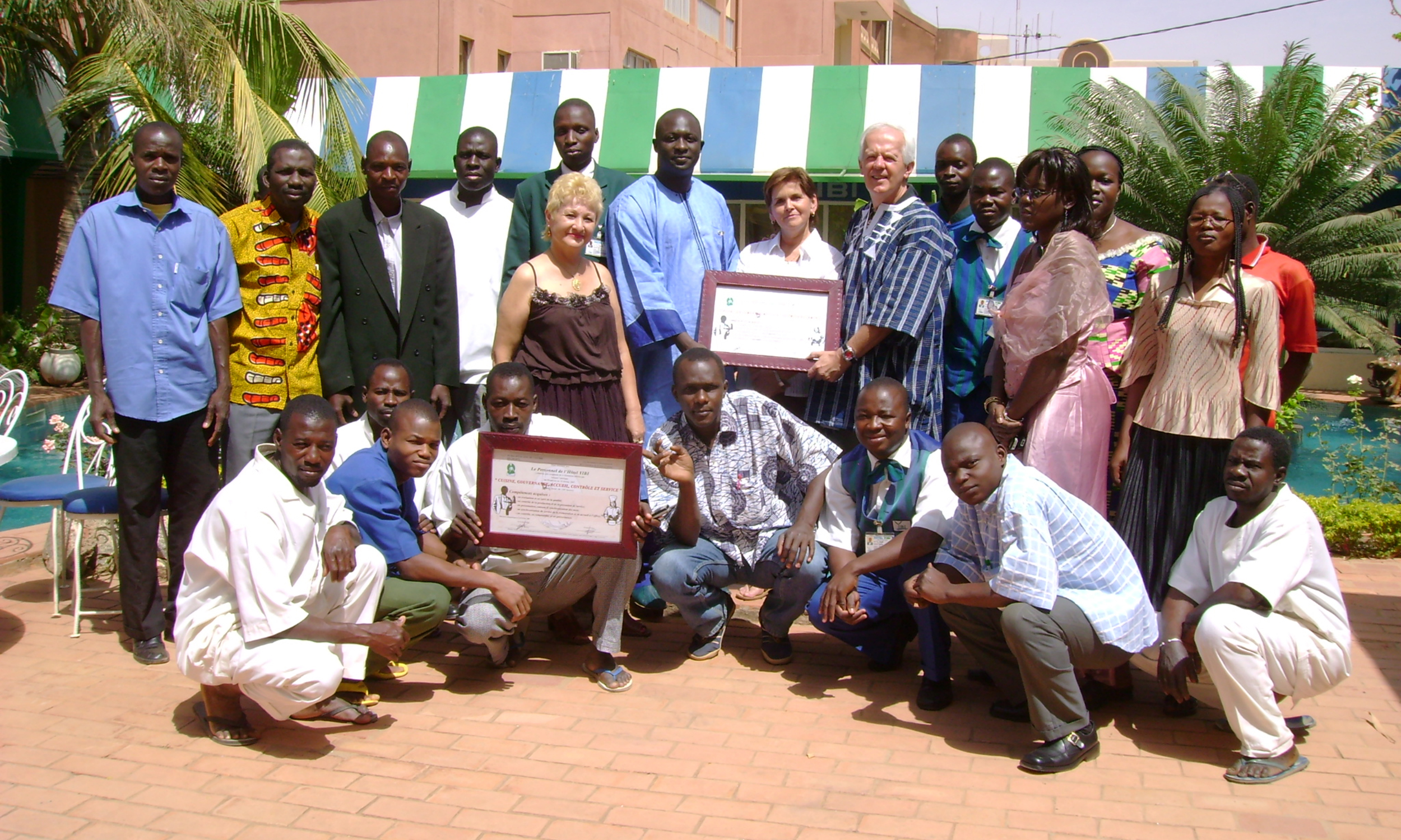 A large group stands outside a striped tent holding framed certificates in Burkina Faso