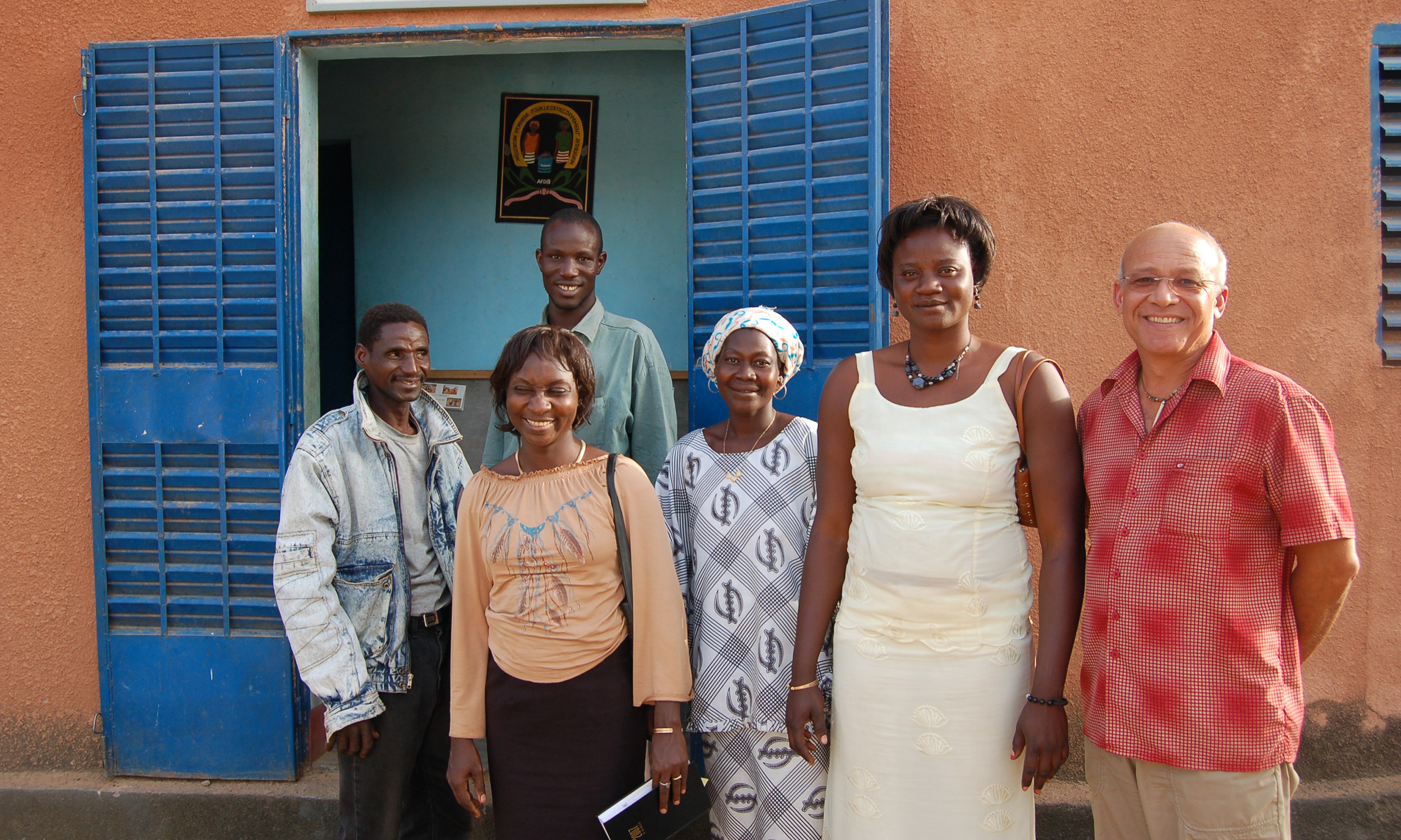 Six smiling people in Burkina Faso stand outside a building with blue shutters