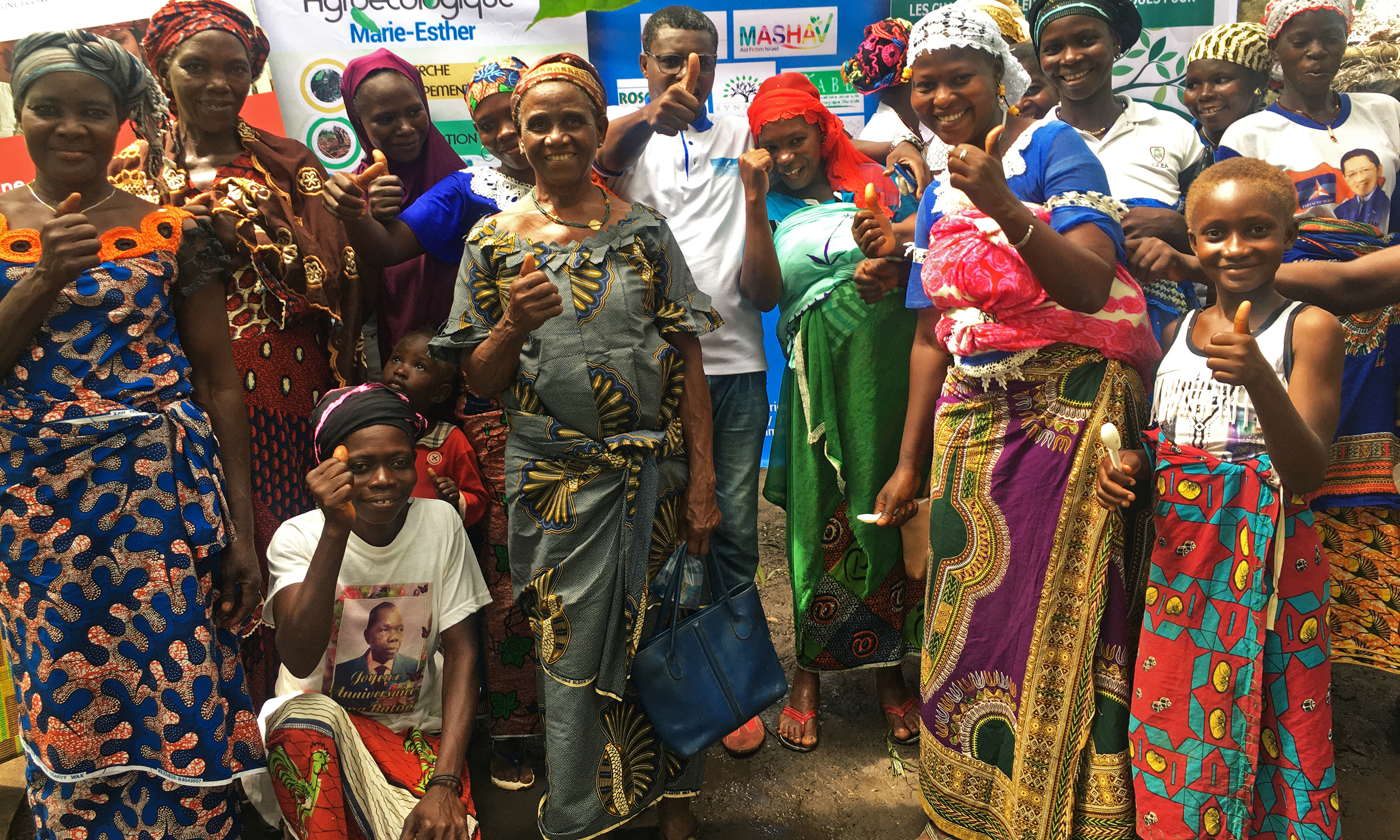 A group of smiling women, men and children in Ivory Coast give a thumbs up
