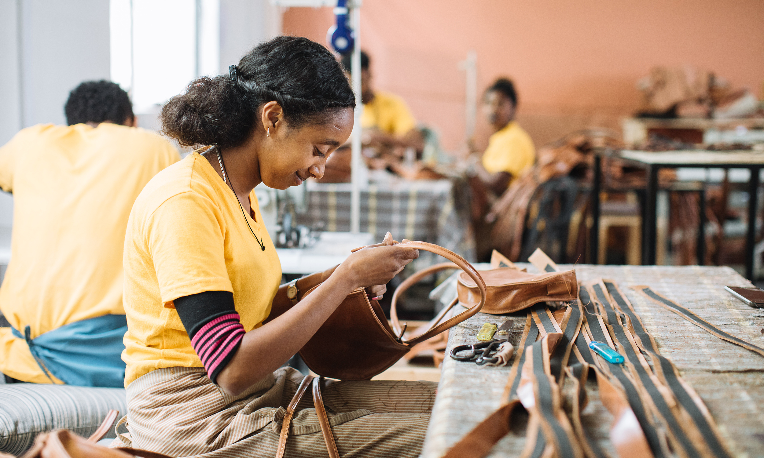 A woman leans over a work table manufacturing a leather good