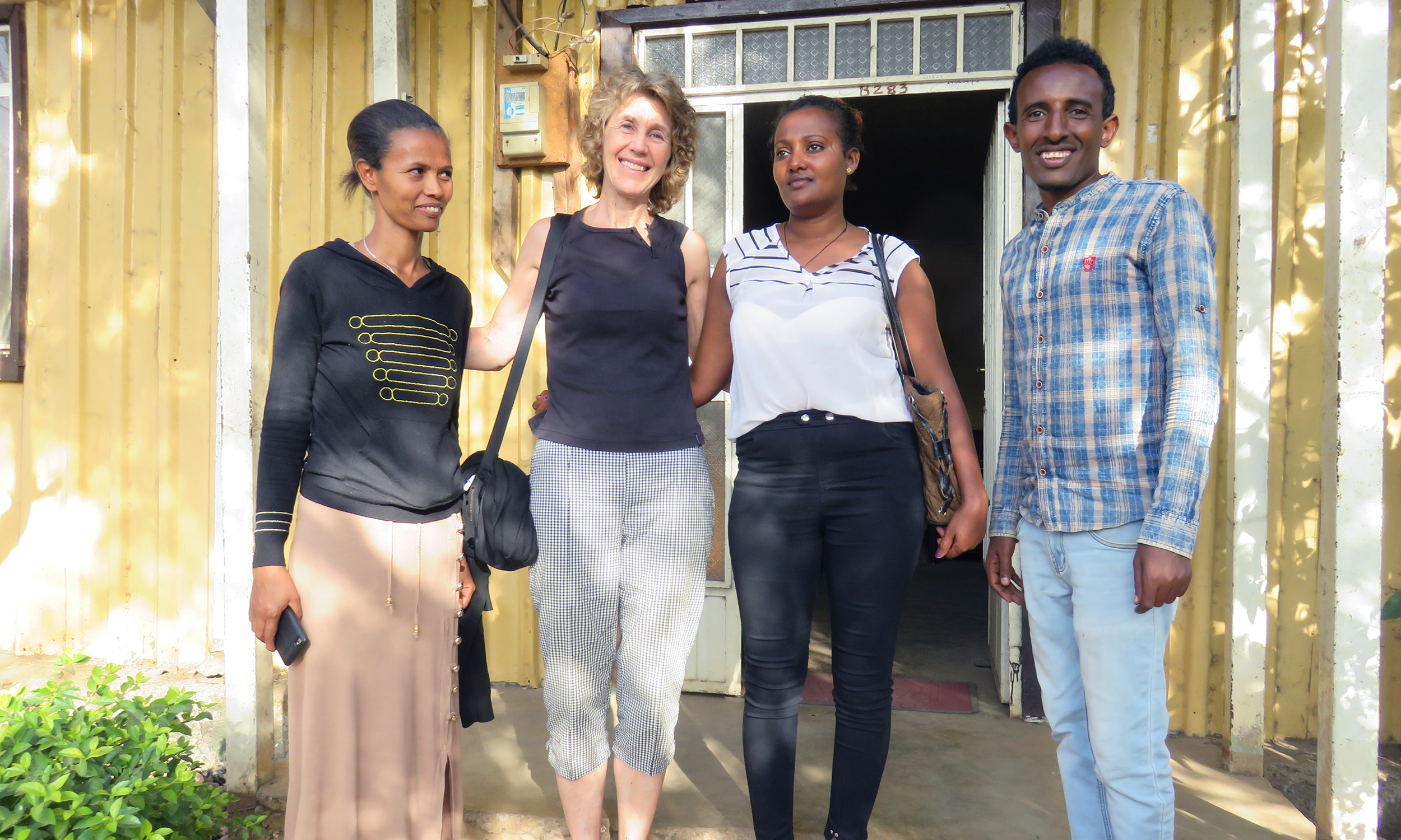 Four people in Ethiopia stand in front of a yellow house