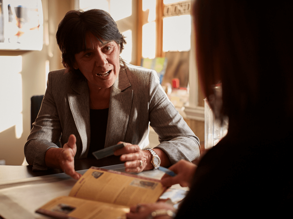 A woman sitting at a table gestures with her hands to another woman