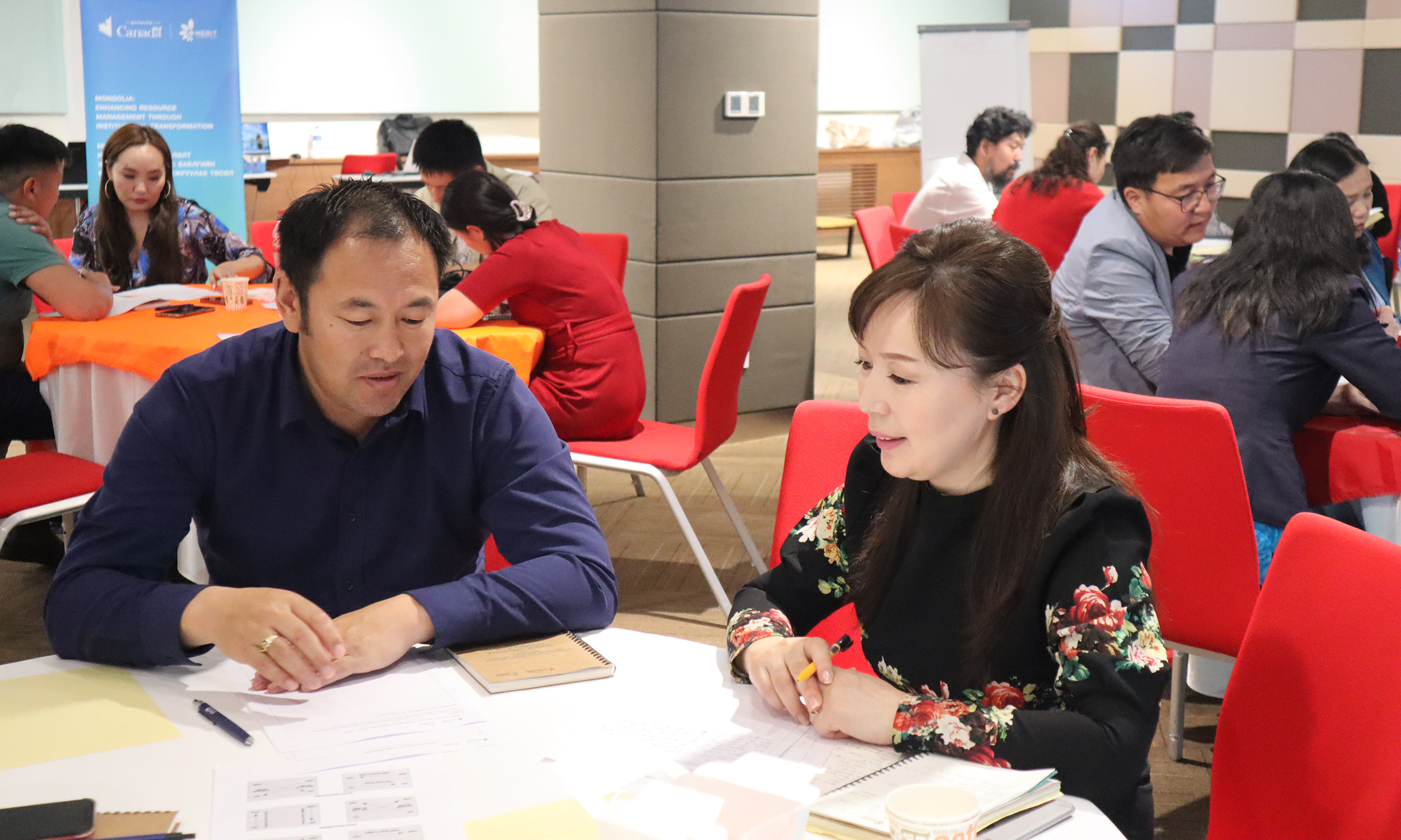 A man and a woman in Mongolia speak together at a table with books on it